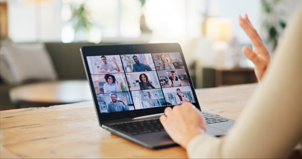 Person waving during a video conference on a tablet with a grid of nine meeting participants